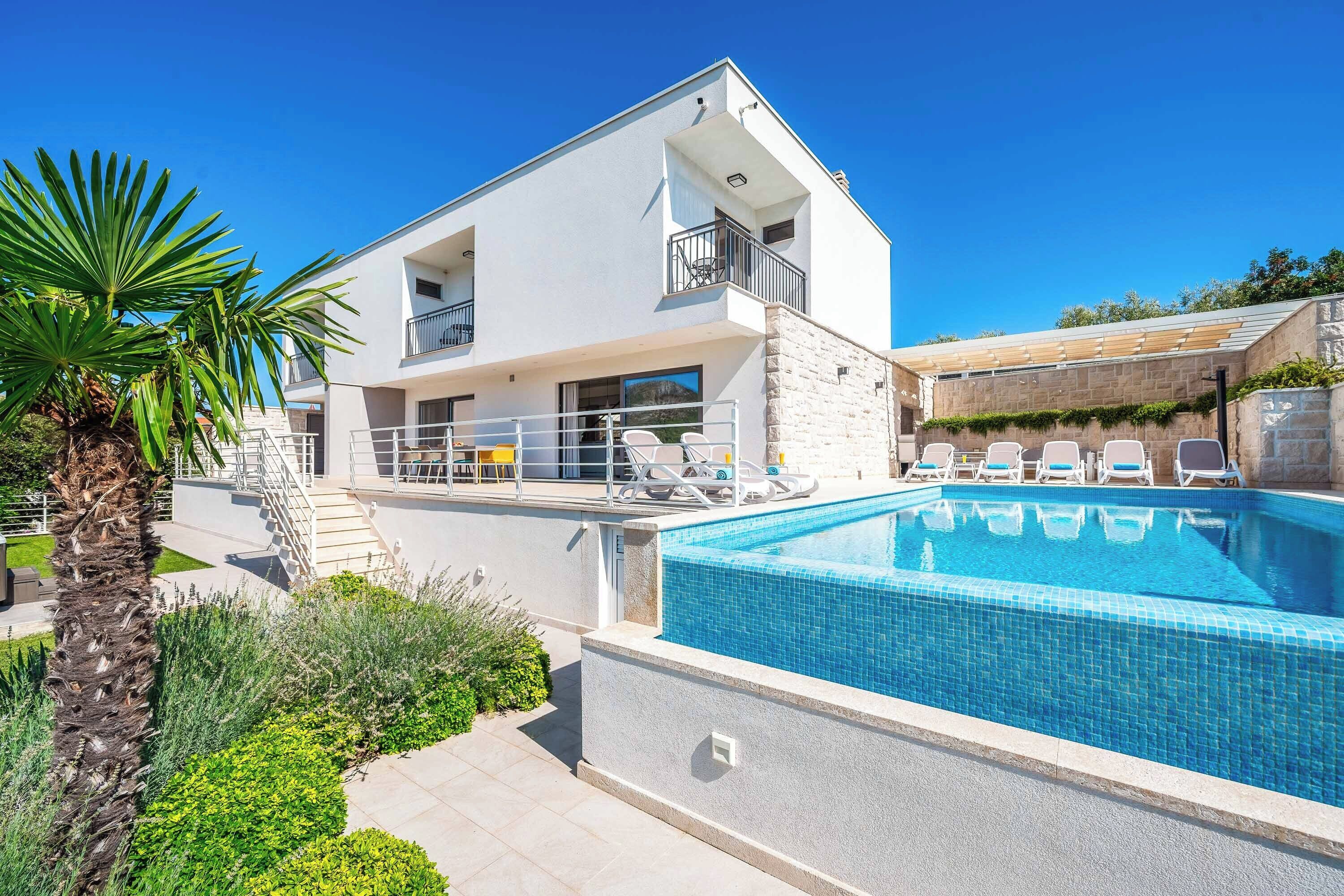 A modern two-story house with a swimming pool, outdoor seating, and a stone wall.