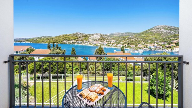 A balcony with a table set for breakfast, overlooking a coastal town with a clear blue sea and hills. - Villa High Life - Four Bedroom Villa, Sleeps 9 (Seget Vranjica)