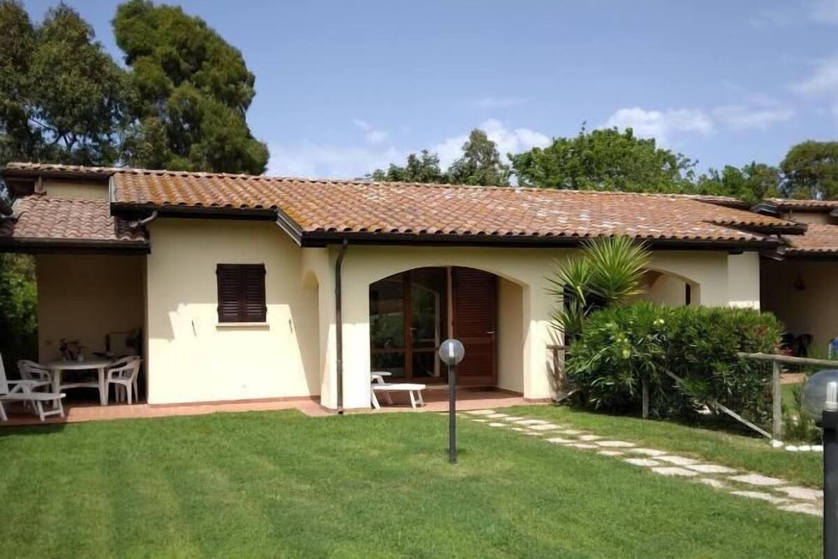 Ein zweistöckiges Haus mit einem Ziegeldach, einer Veranda mit Gartenmöbeln und einem gepflegten Rasen.