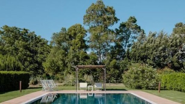 A rectangular swimming pool with a pergola and lounge chairs in the background, surrounded by lush greenery. - Agriturismo Canova - Private Villas (Grosseto)