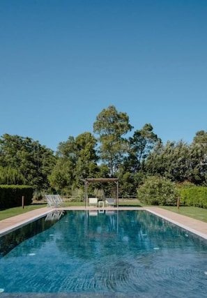 Une piscine rectangulaire, agrémentée d’une pergola et de chaises longues, le tout entouré d’une végétation luxuriante.