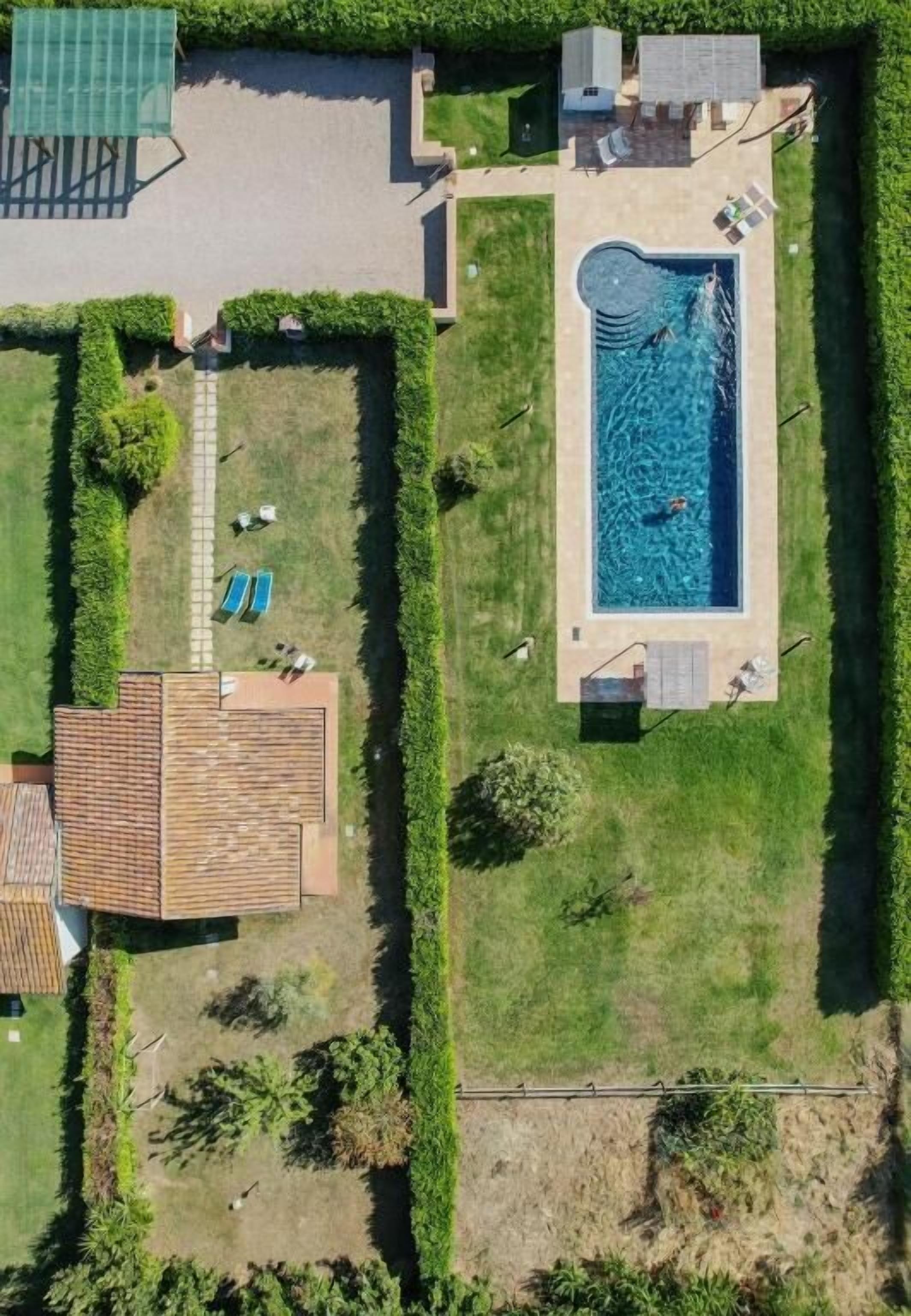 An aerial view of a property with a swimming pool, two sun loungers, a covered patio, and a small building.