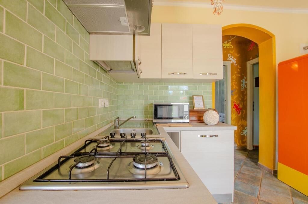 Una cucina con pareti piastrellate in verde, un fornello a gas, un forno a microonde e mobili bianchi.