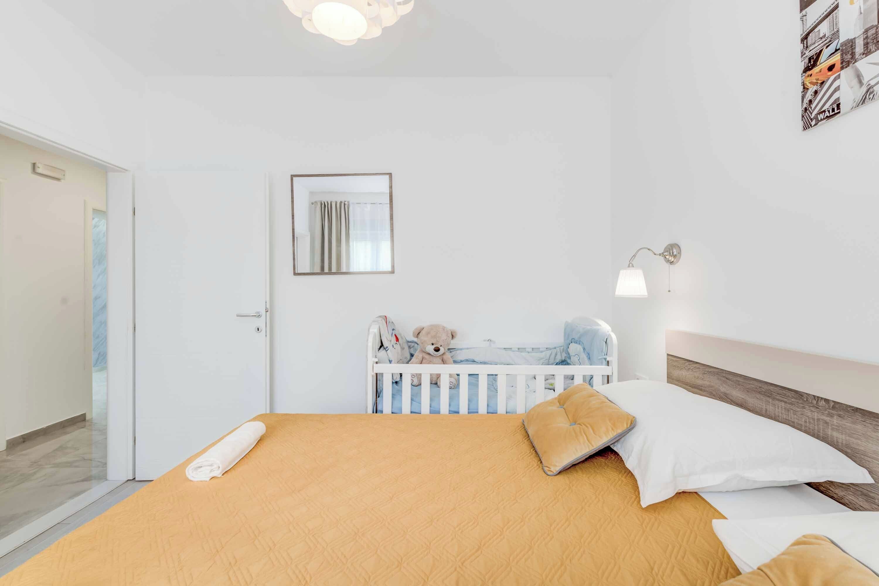 Une chambre à coucher bien rangée, avec un lit, un berceau, un miroir fixé au mur et une lampe de chevet.
