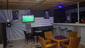 Un área de estar interior con televisión, muebles de mimbre y una barra.