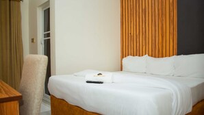 Habitación de hotel con cama, cabecera de madera, una silla y ventana con cortinas.