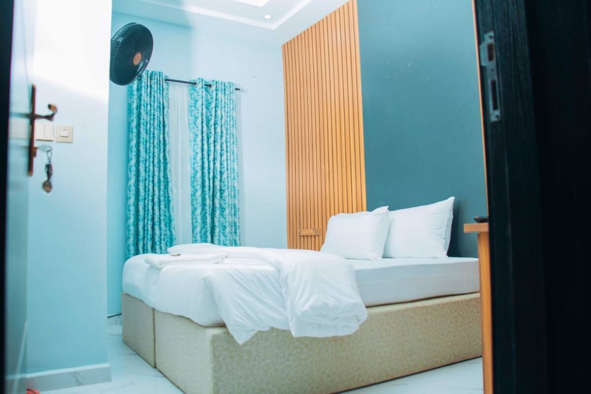 Un dormitorio con cama, ventilador y pared de paneles de madera.