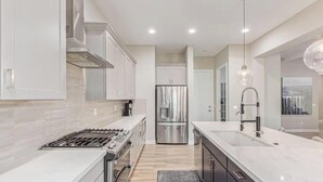 Cozinha moderna com armários brancos, eletrodomésticos de aço inoxidável, uma ilha central com pia e iluminação pendente.