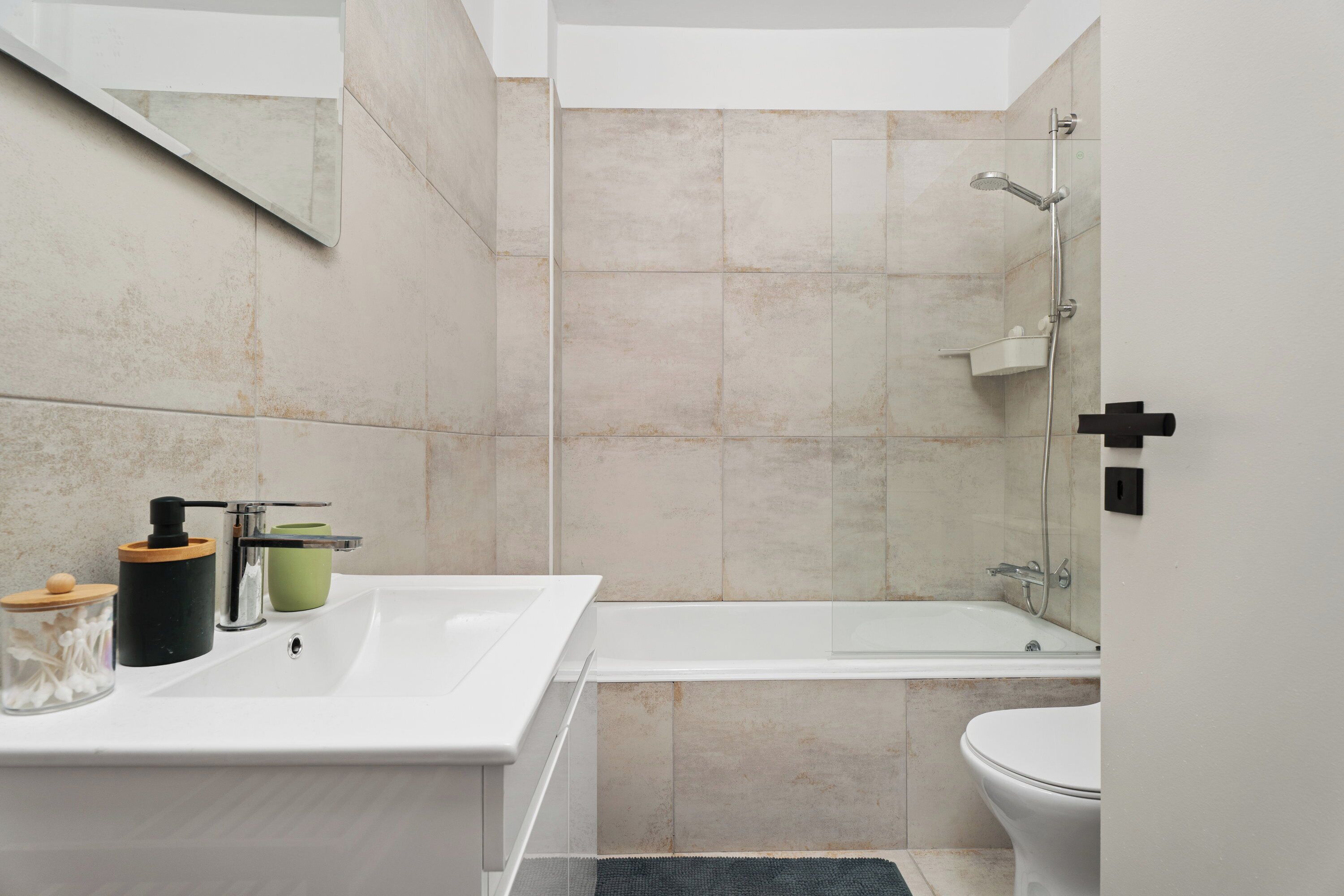 Ein modernes Badezimmer mit einem weißen Waschbecken, einem grünen Seifenspender, einem schwarzen Seifenbehälter, einer weißen Toilette und einer Duschkabine aus Glas.