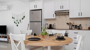 Una cucina moderna con mobili bianchi, un frigorifero in acciaio inossidabile, un tavolo da pranzo con sedie e una pianta in vaso.