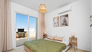 Una camera da letto con un letto, un lampadario, un condizionatore d'aria a parete e una porta scorrevole in vetro che dà su uno spazio all'aperto.