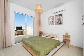 Ein Schlafzimmer mit Bett, einer Pendelleuchte, einer Wand-Klimaanlage und einer Glastür, die zu einem Außenbereich führt.
