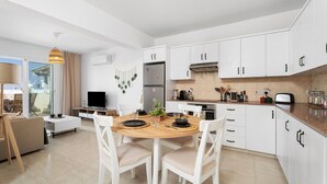 Una cucina moderna con mobili bianchi, un tavolo da pranzo con sedie, una televisione e un balcone con un divano.