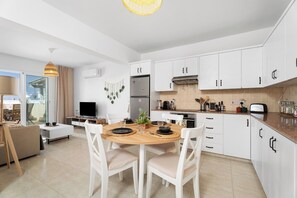 Eine moderne Küche mit weißen Schränken, einem Esstisch mit Stühlen, einem Fernseher und einem Balkon mit einer Sitzecke.