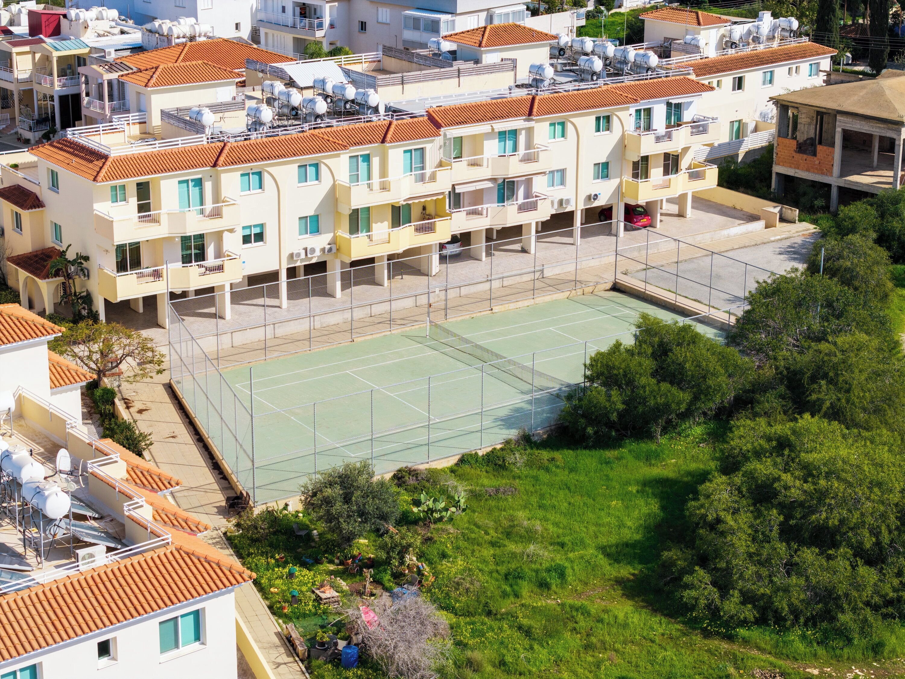 A residential building with multiple balconies, a tennis court, and surrounding greenery.