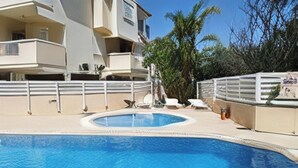 Una piscina con bordo bianco, una palma e un edificio con balconi.