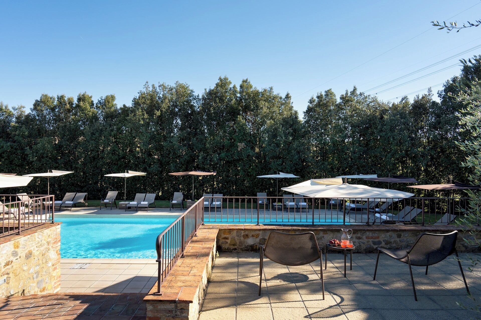 Un espace aménagé au bord de la piscine, avec des chaises longues et des parasols, entouré d’arbres.