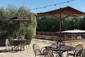 Un espace extérieur aménagé en terrasse, avec des tables et des chaises rondes, des parasols et des guirlandes lumineuses.