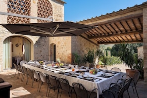 An outdoor dining area with a long table set for a meal, surrounded by stone walls and potted plants. - Villa Le Beringhe 30, Emma Villas (Colle di Val D'Elsa)