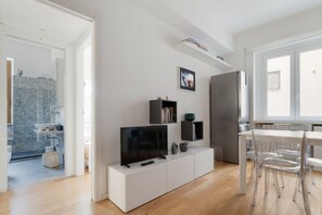 A modern living room with a flat-screen TV, white cabinetry, a dining area with clear chairs, and a kitchen with a refrigerator. - GuestHost - Cozy 50mq apartment perfect for 2 people located on the first floor of a building with lift.The property is located in the Vetra district, located between the columns of San Lorenzo and the Navigli, a historic and fascinating area famous for  (Milan)