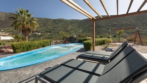 Ein Poolbereich mit Liegestühlen, einer Pergola und Blick auf die umliegende Landschaft.