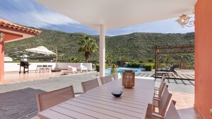 Eine Terrasse im Freien mit Tisch, Stühlen, einem Pool und Blick auf die Berge.