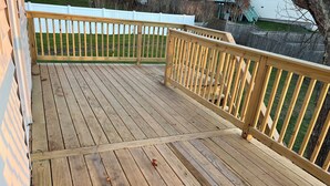 Una terraza de madera con una cerca blanca y un césped al fondo.
