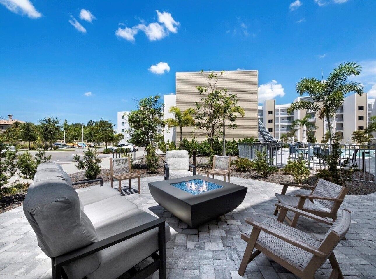 An outdoor patio with a fire pit, lounge chairs, and a pool area in the background.