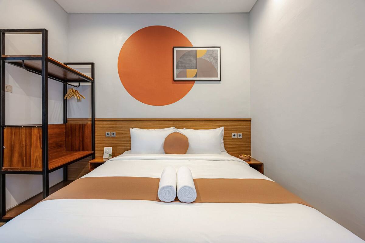 Habitación de hotel con cama, cabecero de madera, una obra de arte en la pared y un diseño circular.