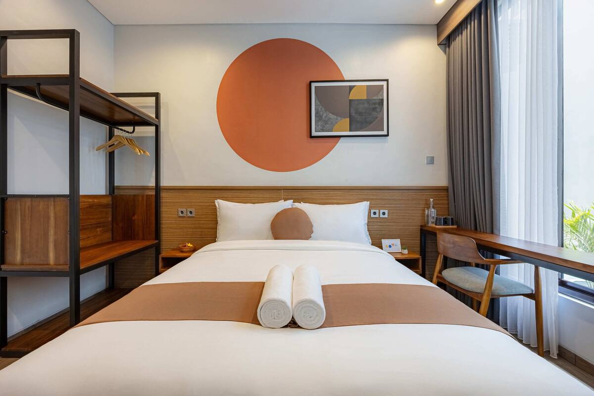 Habitación de hotel con cama, escritorio, silla, armario y un gran adorno circular en la pared.