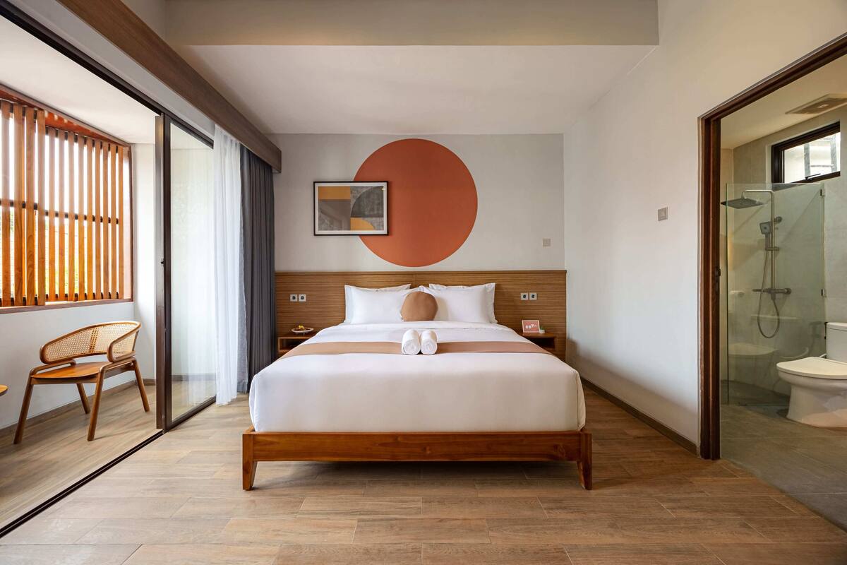 Una habitación de hotel moderna con una cama grande, suelo de madera, cabina de ducha de vidrio y un gran adorno circular en la pared.