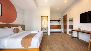 A modern hotel room with a large bed, a wooden headboard, a bedside table, a TV, and a bathroom visible through an open door.