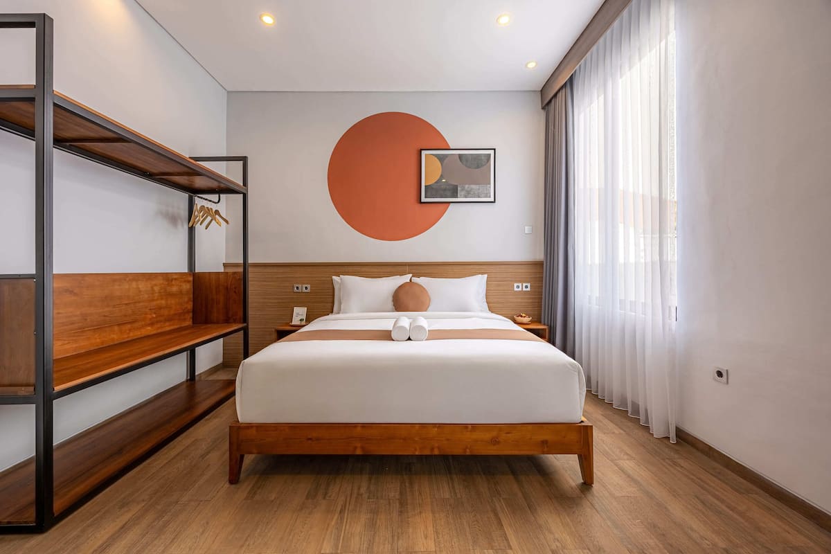 Una habitación de hotel moderna con una cama de madera, un adorno circular grande en la pared, una mesita de noche y un banco empotrado con espacio de almacenamiento.