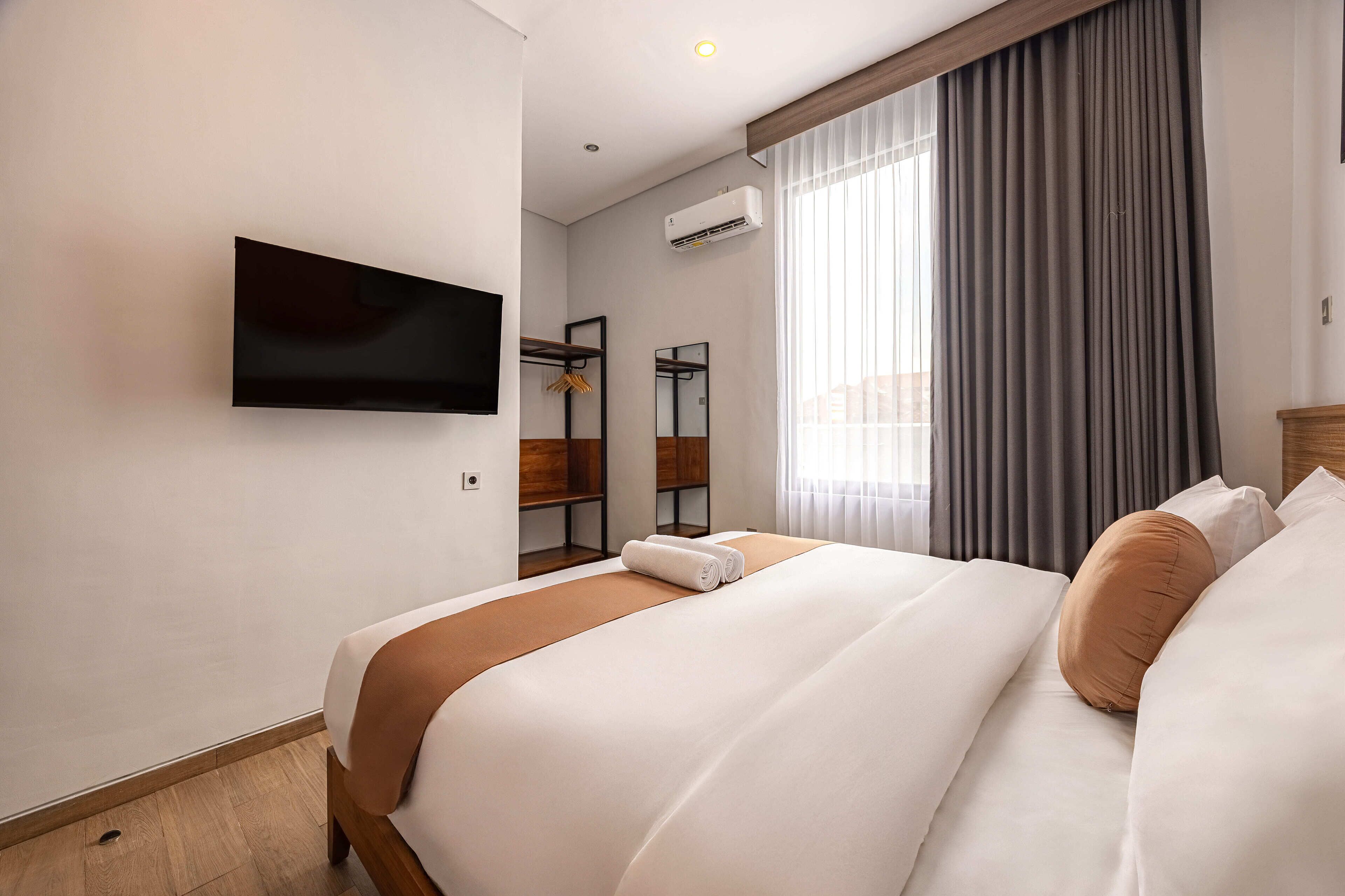 A hotel room with a bed, a TV mounted on the wall, a mirror, and an air conditioning unit.