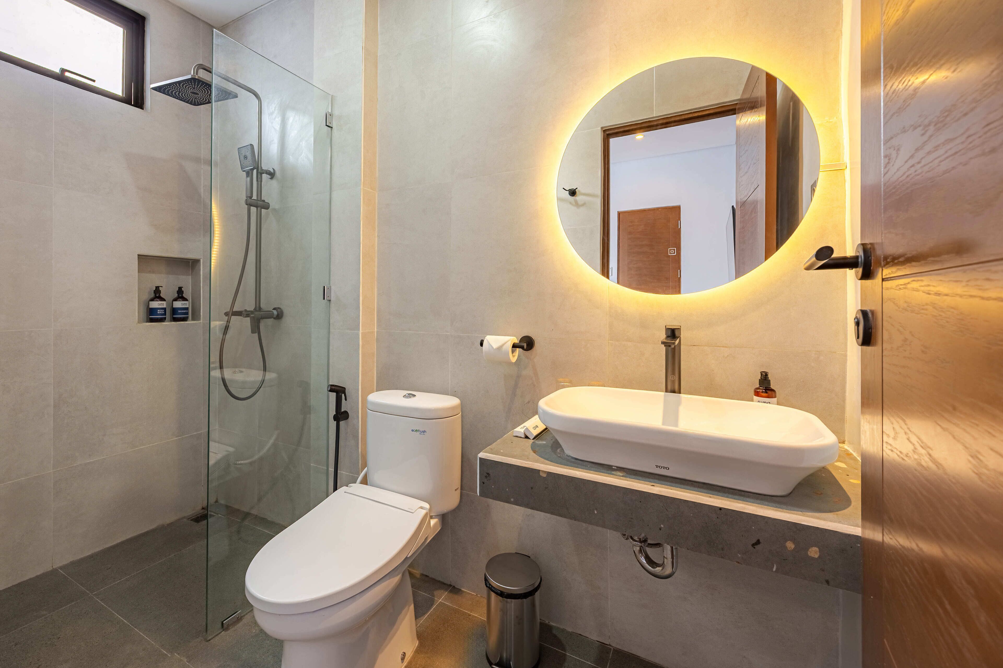 Een moderne badkamer met een glazen douchecabine, toilet, wastafel met spiegel en een prullenbak.