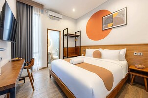 A hotel room with a large bed, a wooden desk, a chair, a small table, and a wall-mounted shelf.