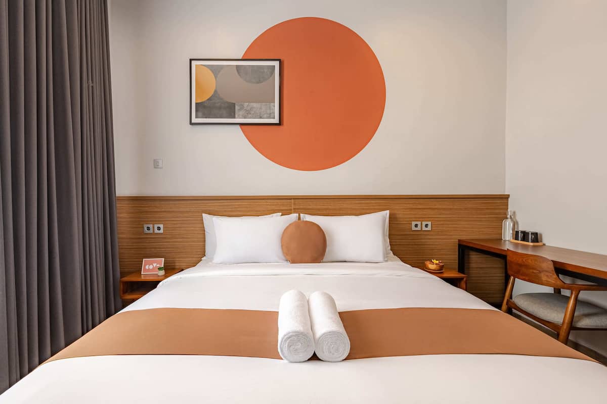 Habitación de hotel con una cama grande, cabecera de madera, un escritorio con silla y una pared con un círculo naranja grande.