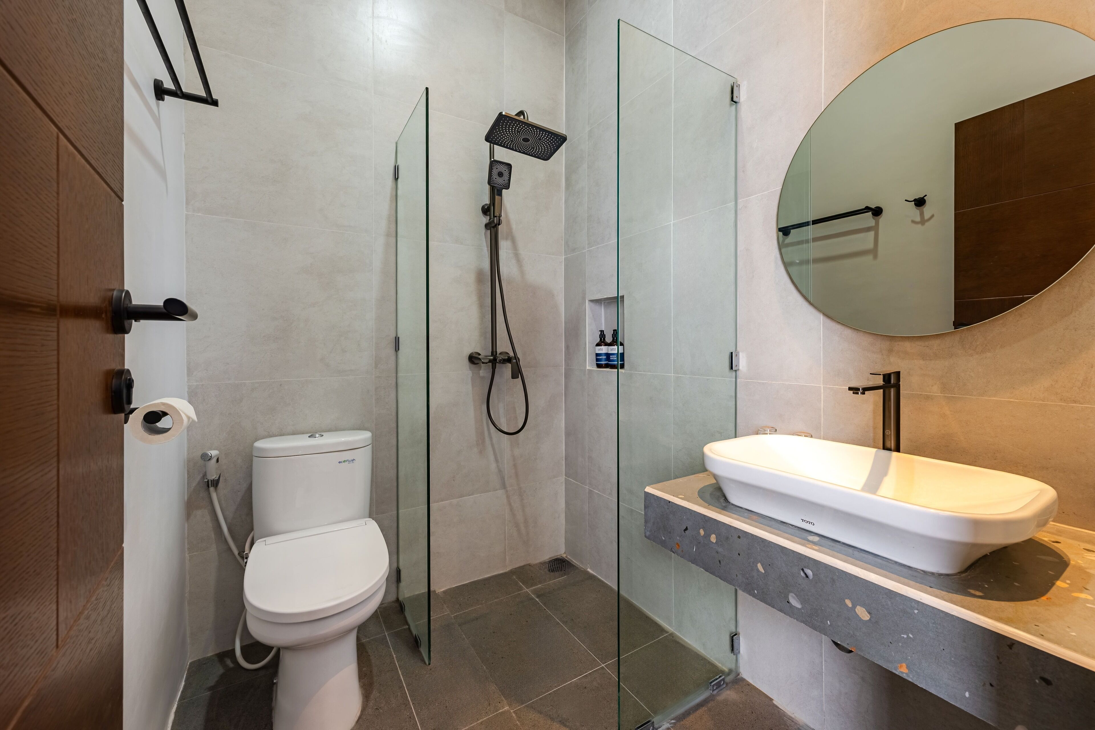 A modern bathroom with a glass-enclosed shower, a toilet, and a sink with a mirror above it.