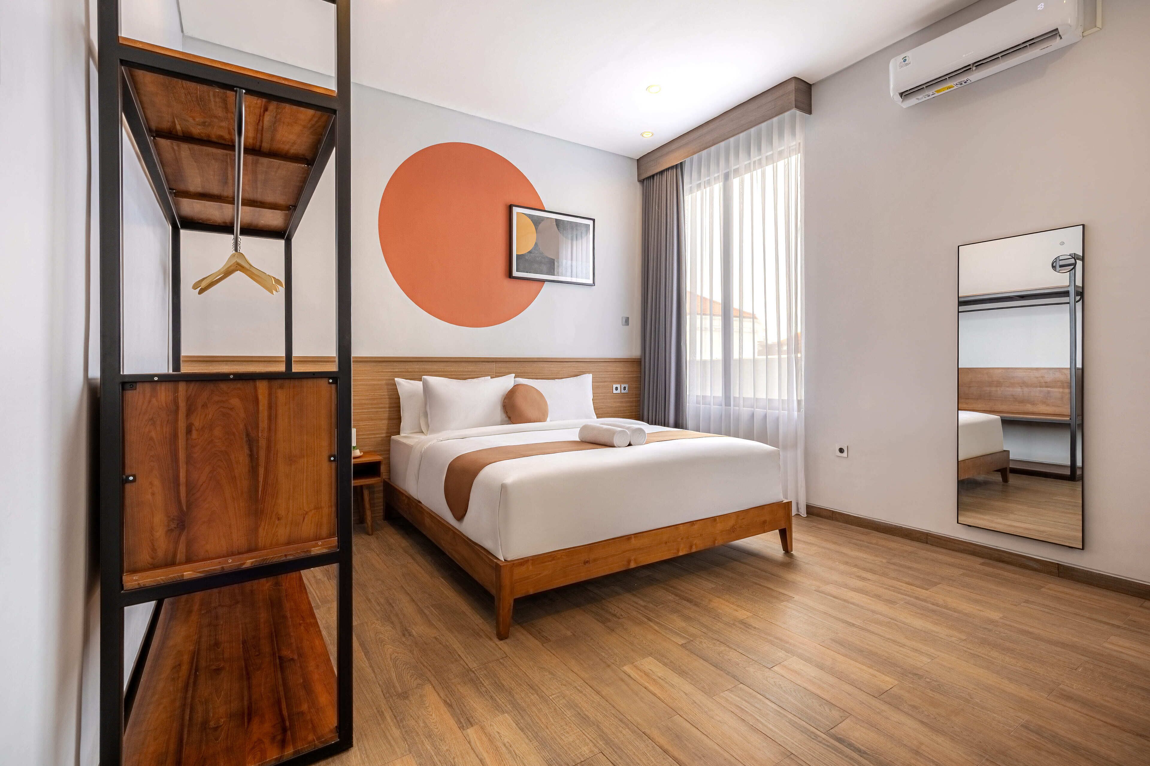A modern hotel room with a wooden bed, a large mirror, and a wall-mounted air conditioner.