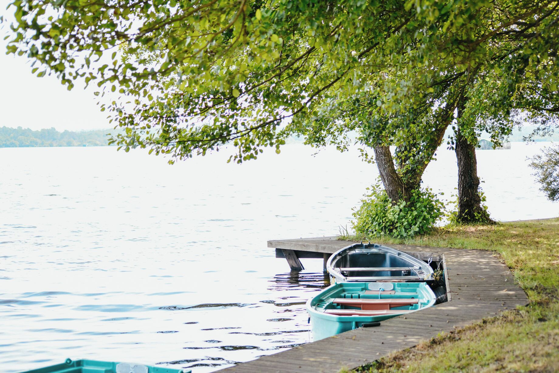A dock with a rowboat and a small boat tied to it, overlooking a calm lake.