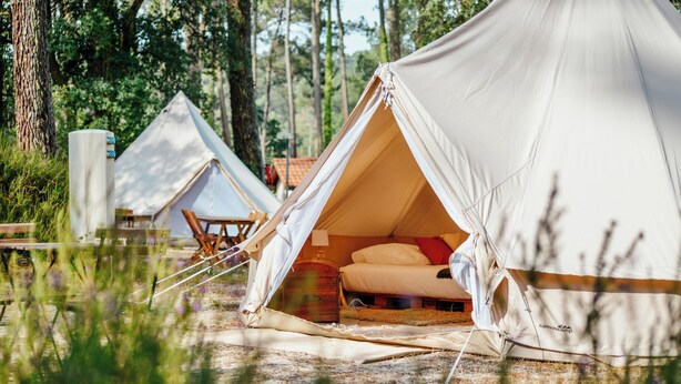 Een linnen tent met een bed, omgeven door een bos.