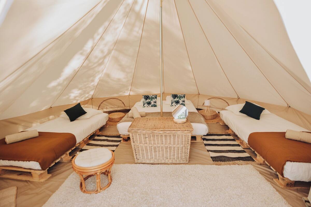 A cozy tent with two beds, a central seating area, and a small stool.