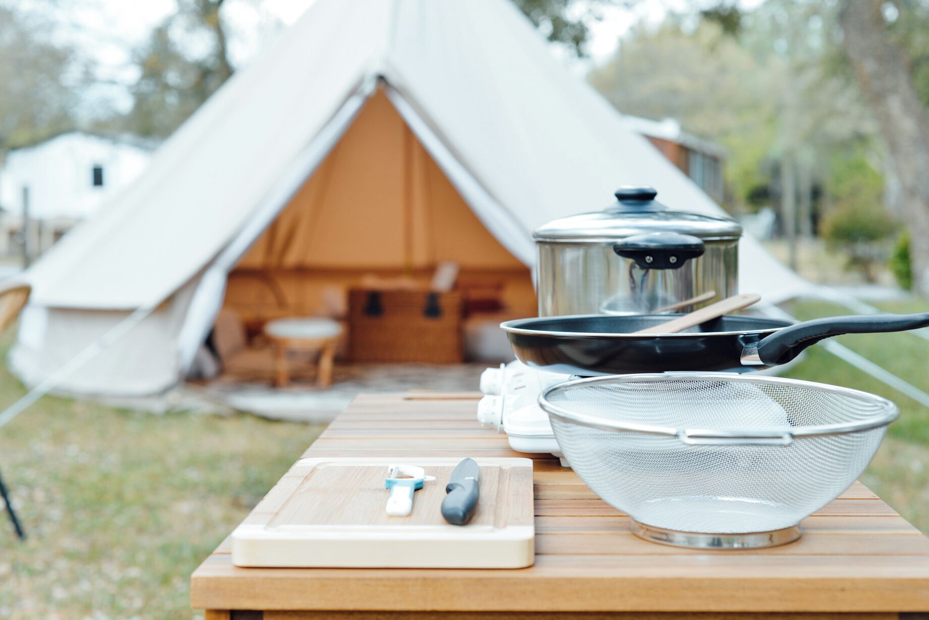 Un équipement de camping comprenant une tente, du matériel de cuisine et une planche à découper avec des ustensiles.