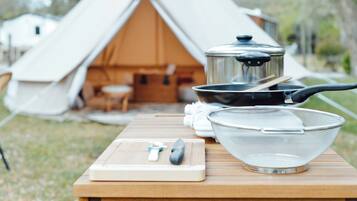 Un équipement de camping comprenant une tente, du matériel de cuisine et une planche à découper avec des ustensiles.