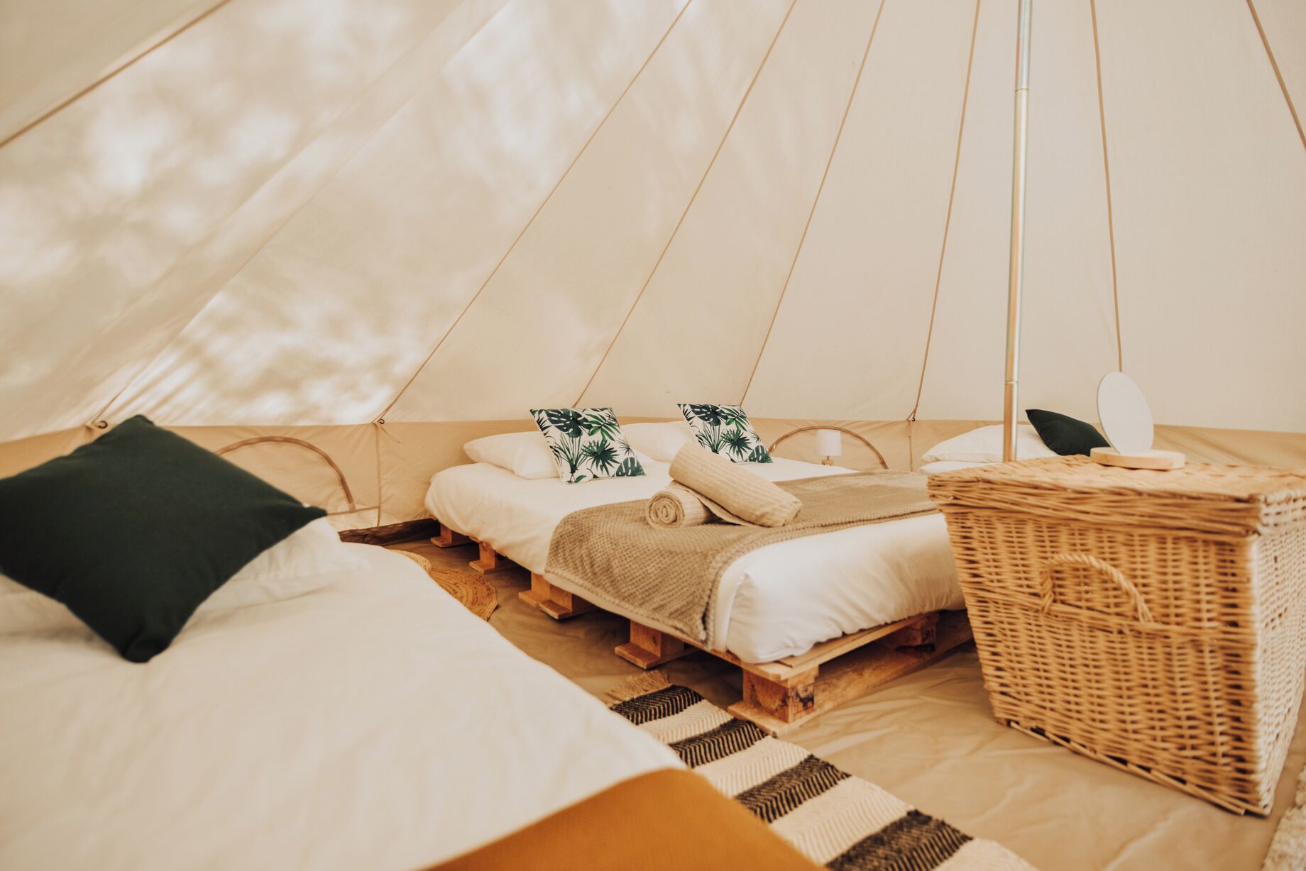 Een gezellige tent met een bed, kussens, een klein tafeltje en een rieten mand.