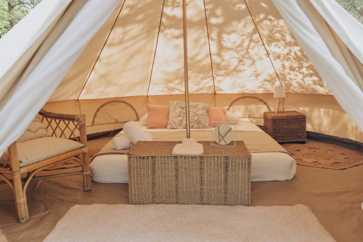 A cozy tent with a bed, pillows, a wicker table, and a chair.