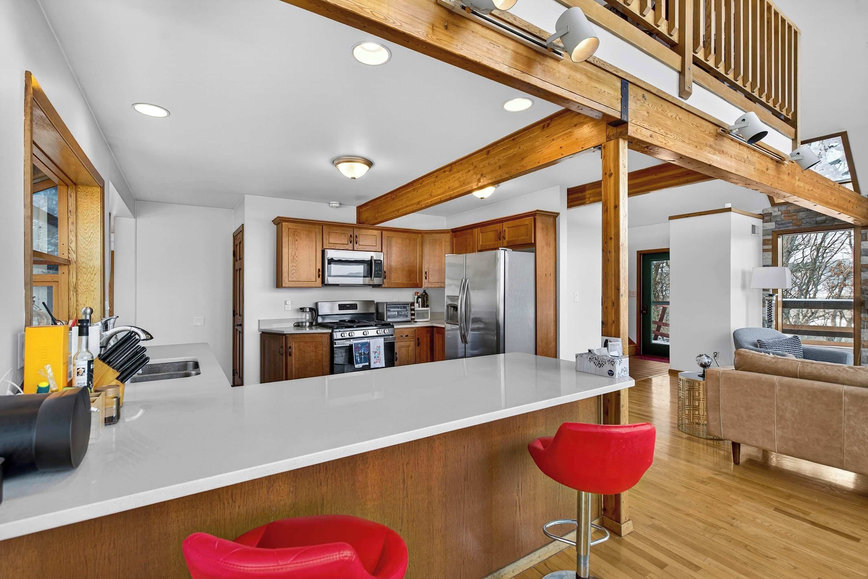 A modern kitchen with wooden beams, a central island, and red bar stools.