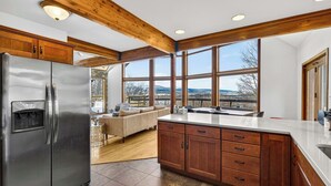 A modern kitchen with wooden beams, large windows, a refrigerator, and a dining area with a view.