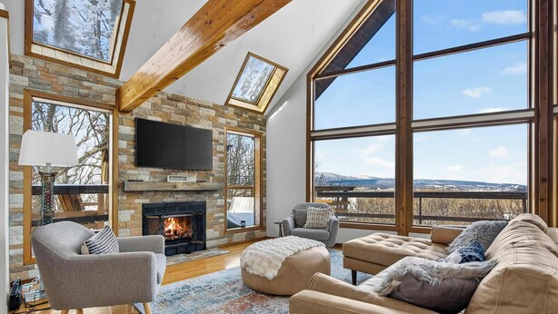 A spacious living room with a stone fireplace, large windows, and a cozy seating area.