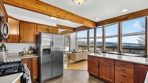 A modern kitchen with wooden cabinets, a stainless steel refrigerator, and a large window offering a view of the outdoors.